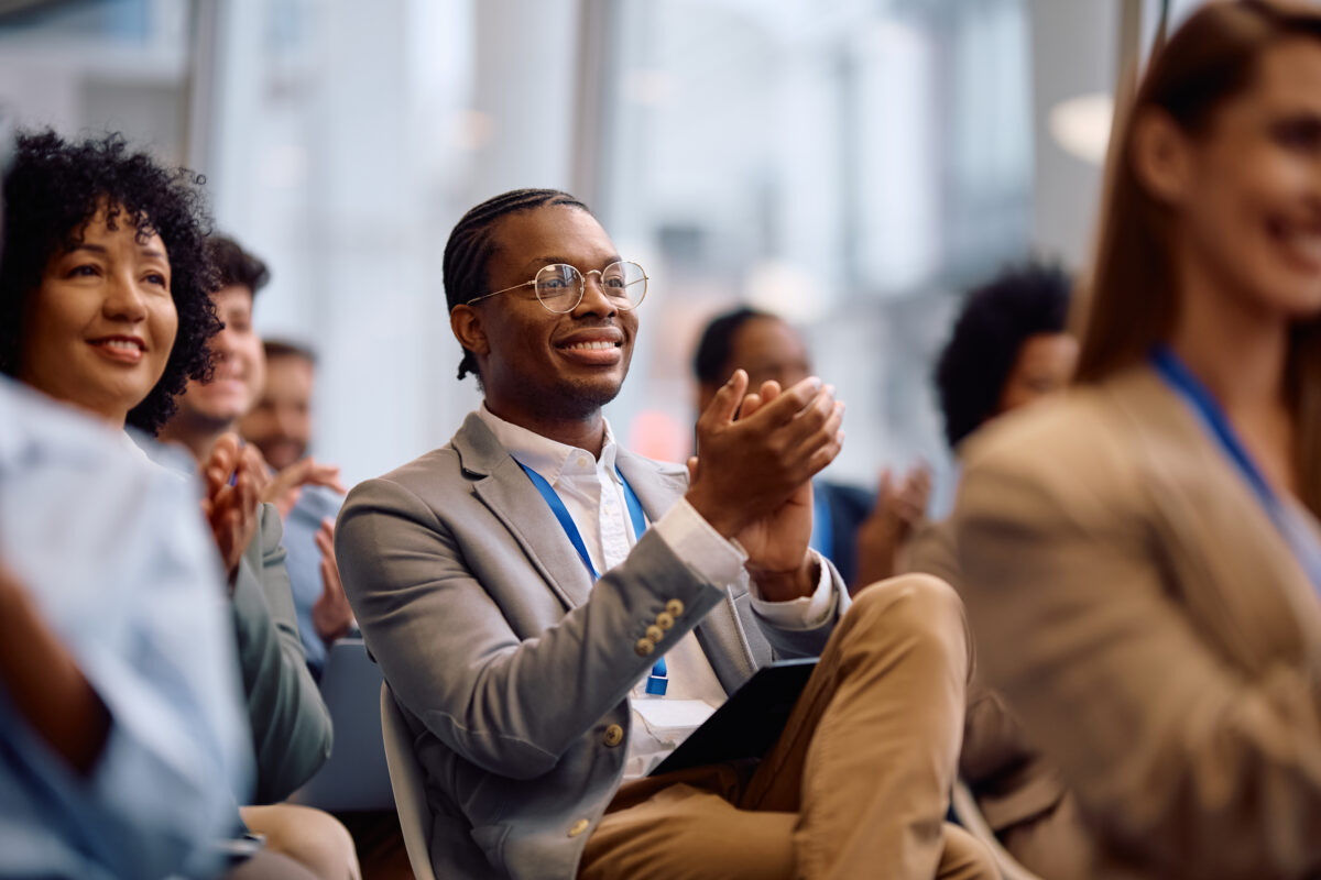 Happy black businessman applauding on education event at conference hall.