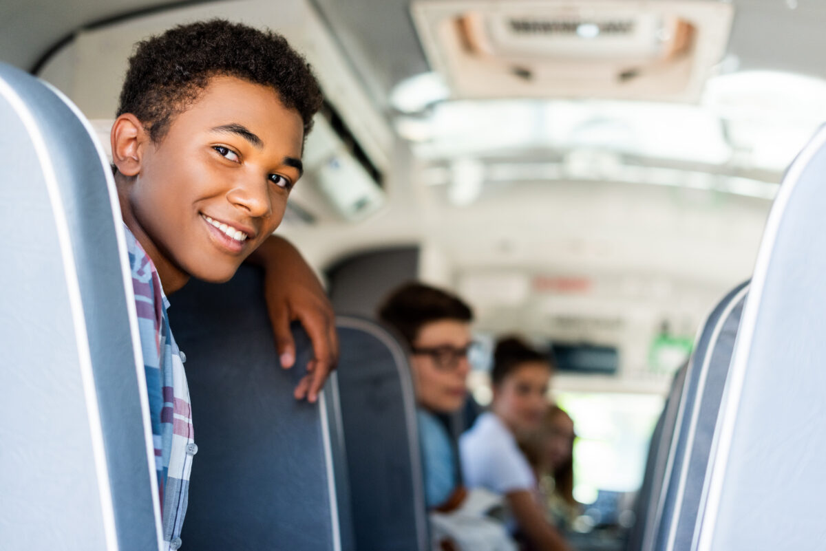 Teen students sitting at school bus and looking back at camera